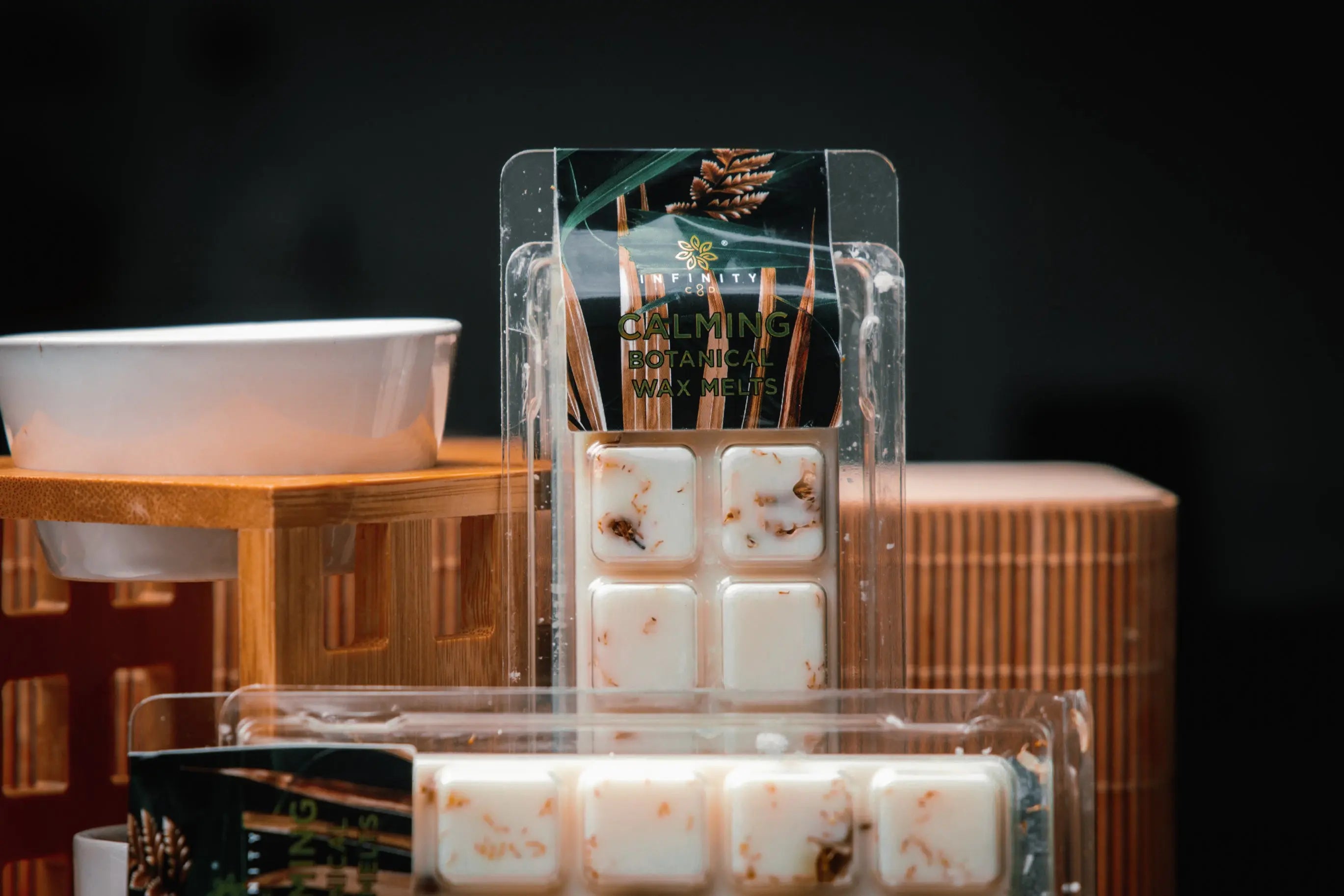 Essential oil wax melt burner cbd wax melts A white ceramic essential oil burner with a dish on top, surrounded by botanicals. A lit tea light candle can be seen beneath